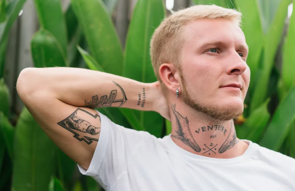 Homme stylé avec tatouage temporaire serpent visible au poignet et cou en ambiance plage