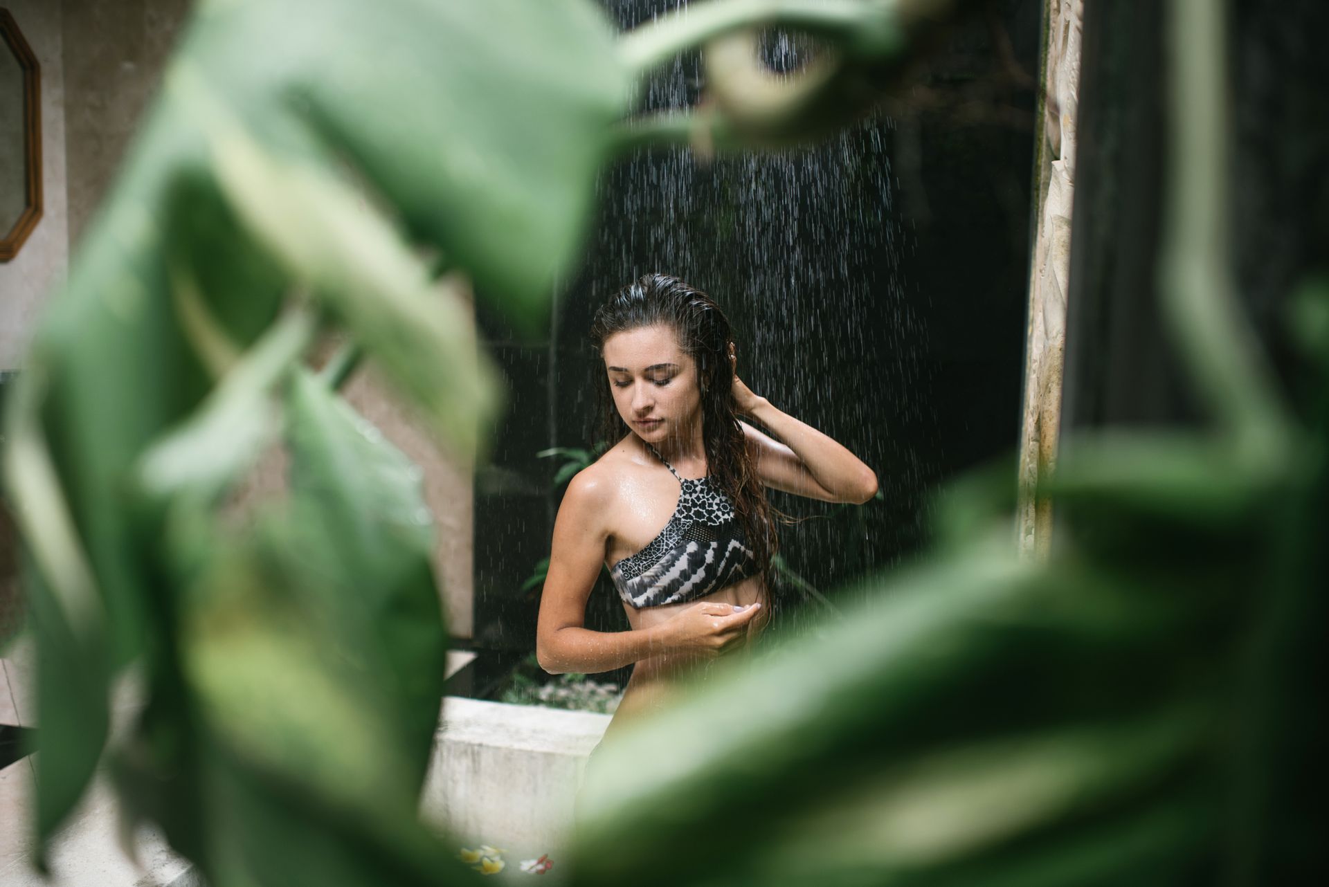 A serene woman enjoys a tropical outdoor shower surrounded by lush greenery.