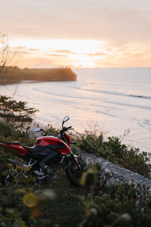 Modern red motorbike left on green seashore with amazing view on calm sea at sunset