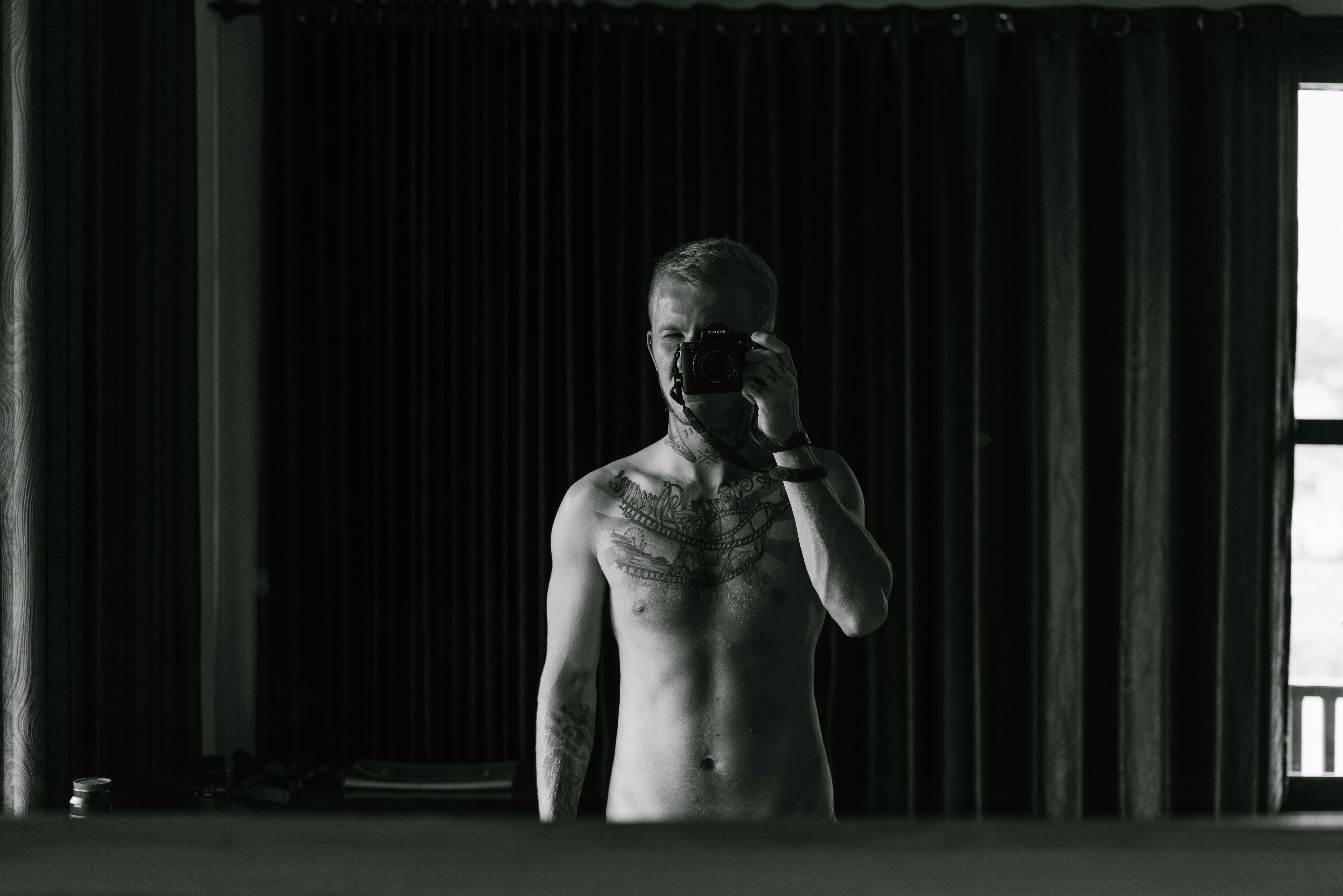 slim anonymous tattooed male taking photo in mirror