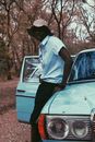 Young black man leaning on blue retro car