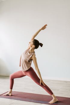 A woman performs a yoga pose indoors, showcasing strength and flexibility on a yoga mat.