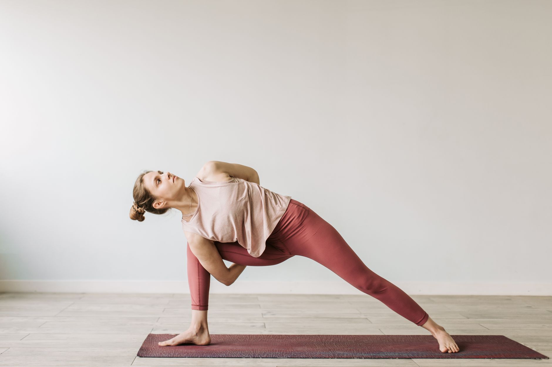 瑜珈墊如何助你找回內在平靜?實用指南與益處 A woman practicing a yoga pose indoors on a mat, showcasing flexibility and wellness.