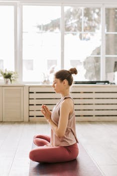 Woman meditating indoors in a seated yoga pose at home with natural light.