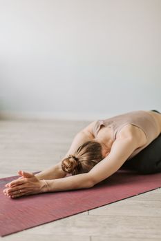 A woman performing a relaxing child's pose on a yoga mat indoors, promoting wellness and flexibility.