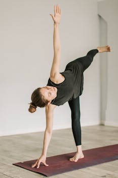 An adult woman practicing yoga indoors, balancing on a yoga mat for wellness and fitness.