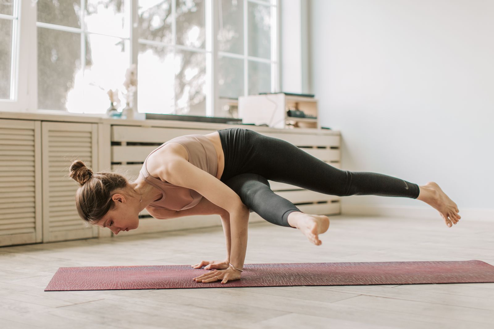 Woman practicing an advanced elbow-supported arm balance yoga pose on a mat indoors