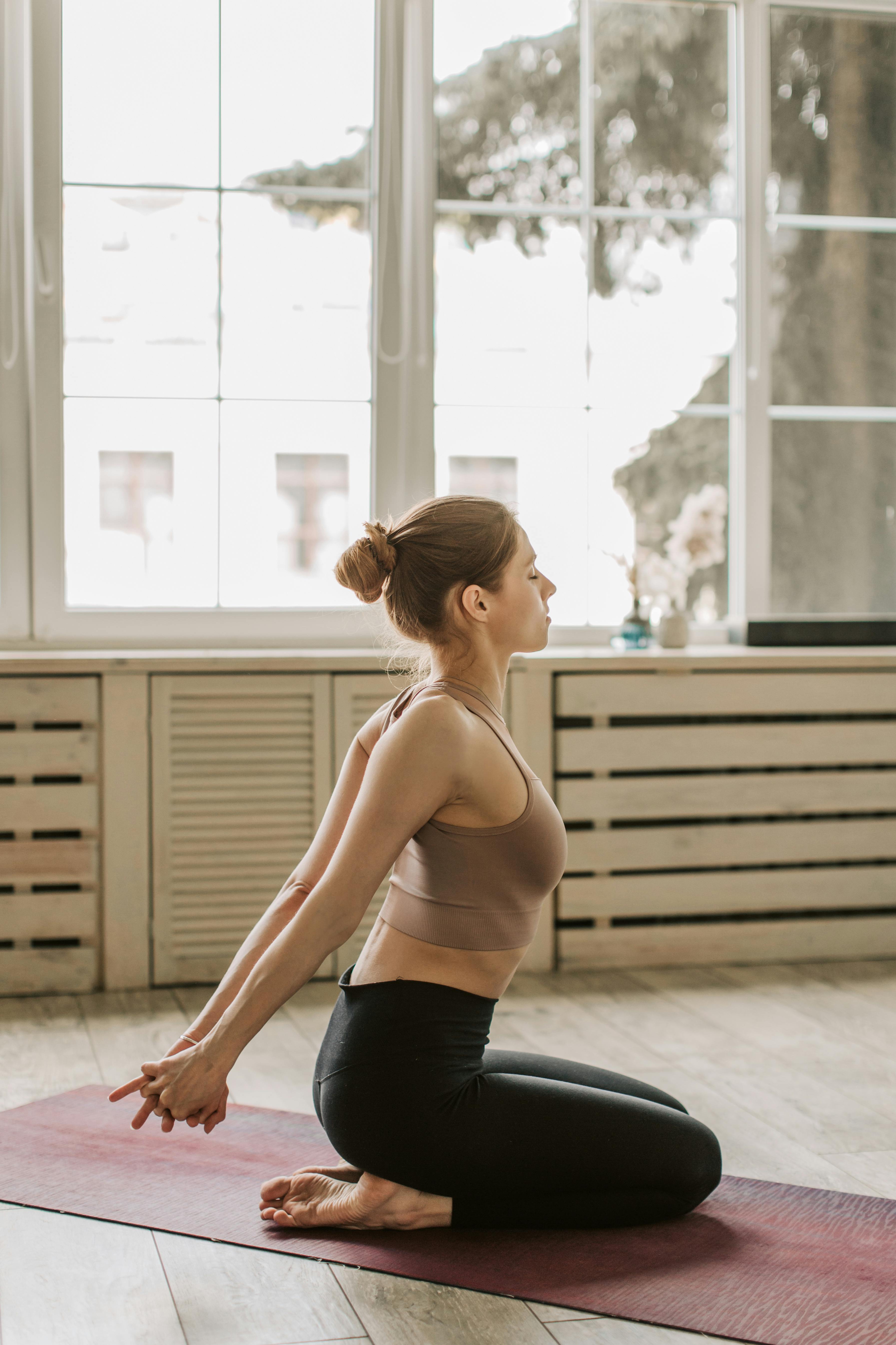 Woman performing a yoga pose indoors by a window, embodying calmness and flexibility.