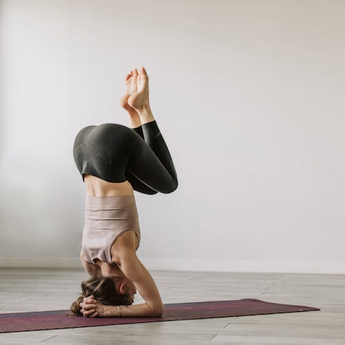 Woman in Black Leggings and Sports Bra Balancing on a Yoga Mat Using Her Head