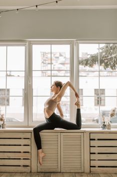 Flexible woman performing yoga pose on a windowsill, showcasing balance and wellness.