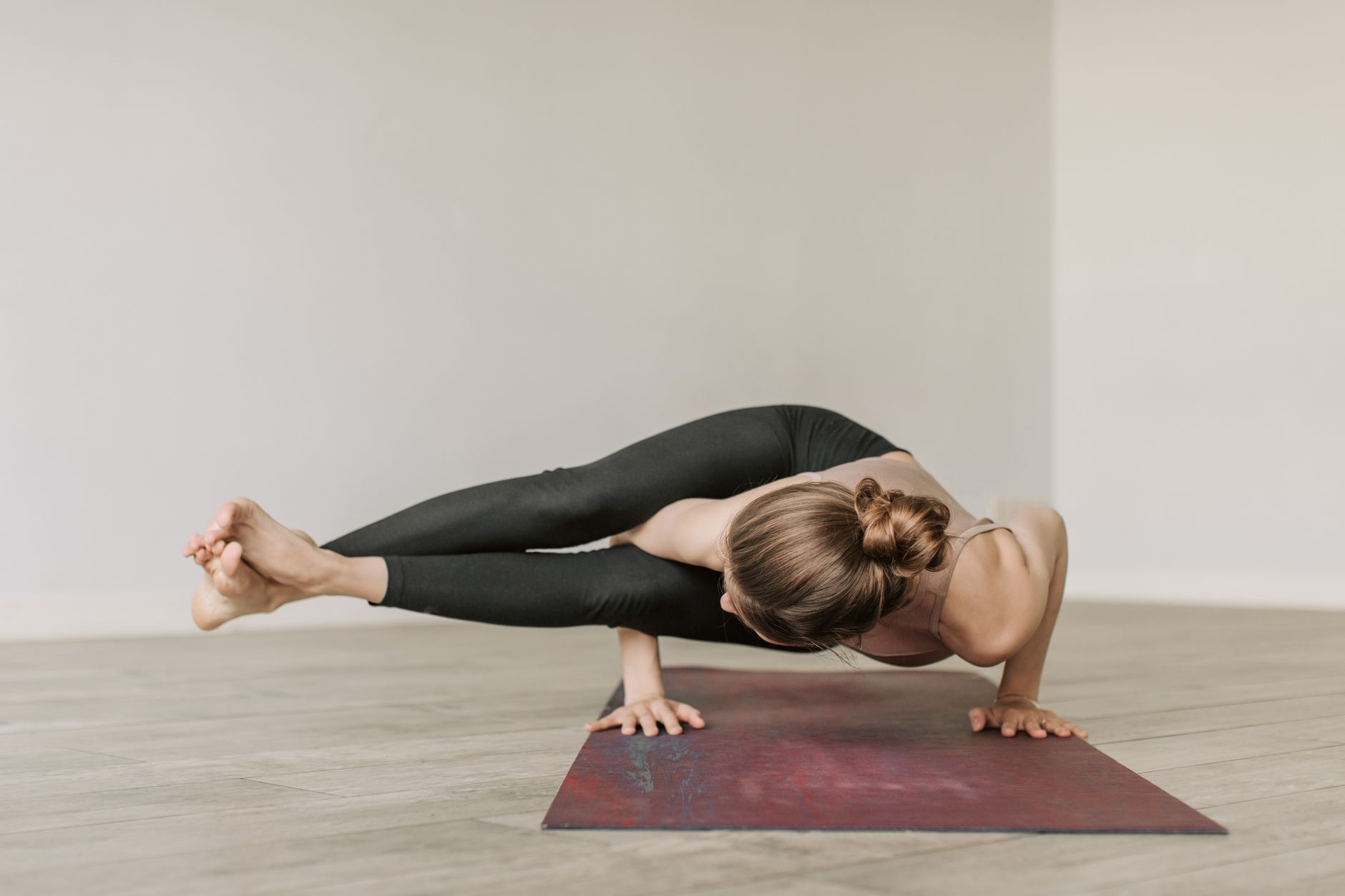 Adult woman practicing an advanced yoga pose on a mat indoors, showcasing flexibility and balance.