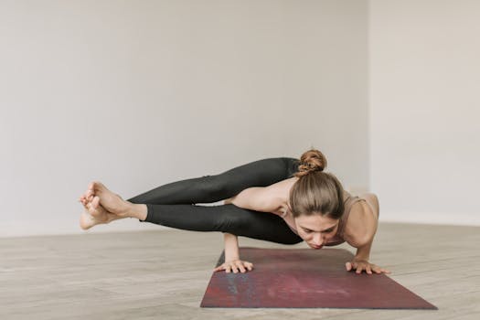 Woman performing a complex yoga pose on a mat indoors, showcasing strength and flexibility.