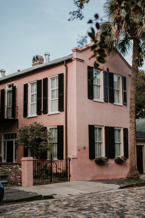 Free A picturesque pink house with black shutters and a palm tree, perfect for urban architectural themes. Stock Photo