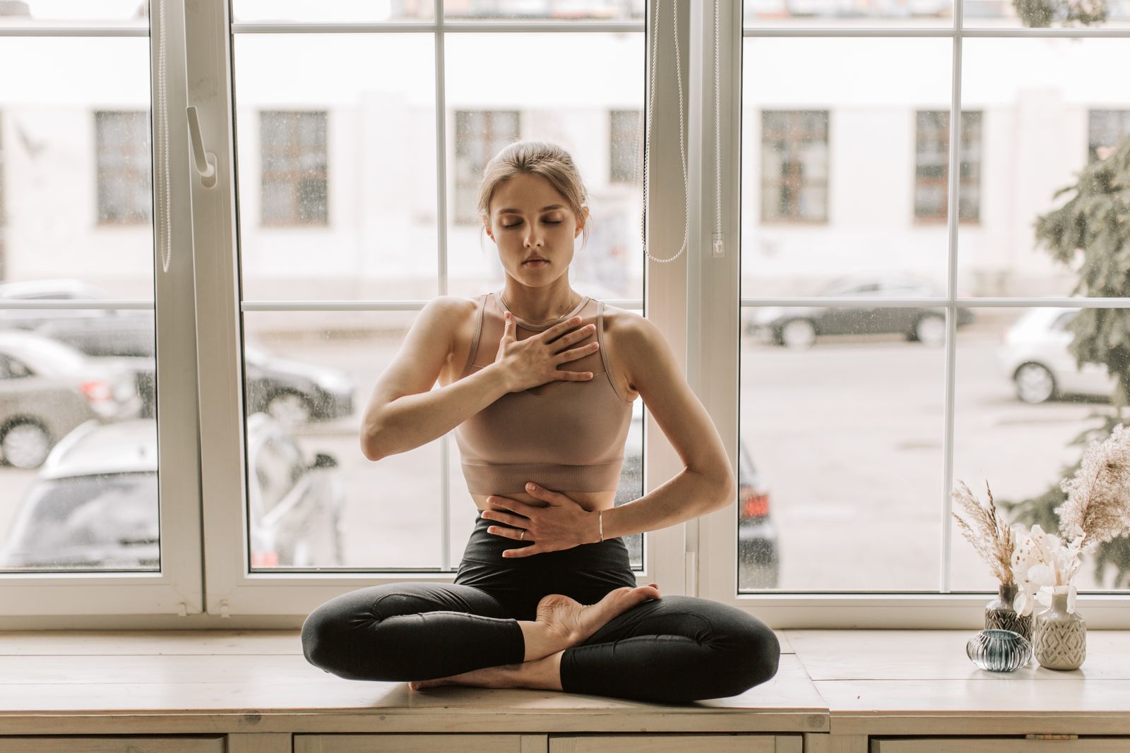 Woman practicing calming seated yoga breathing pose by a window, part of a yoga for fatty liver routine