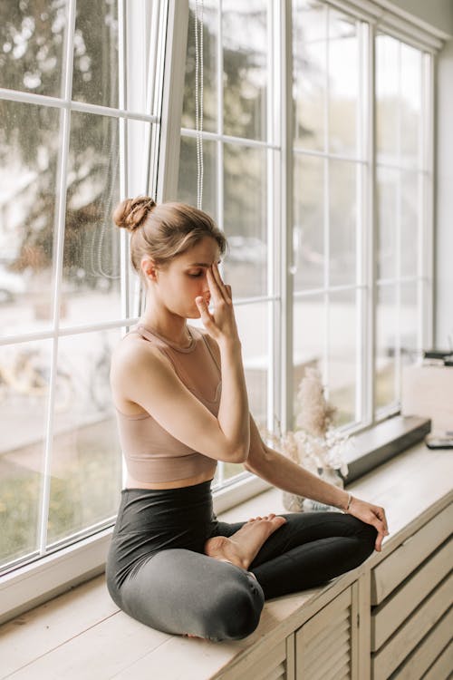 Free A Woman in Black Leggings Sitting Near the Window while Meditating Stock Photo