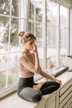 A woman meditating in a yoga pose on a windowsill, embracing wellness and tranquility.