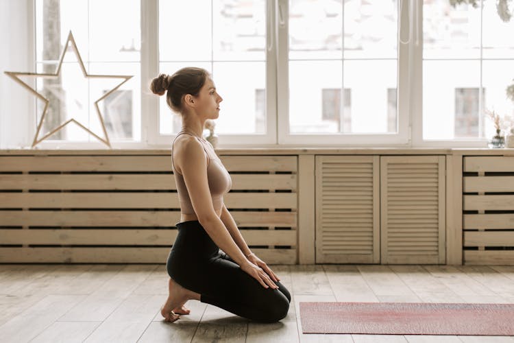 A Woman In Beige Tank Top And Black Leggings Kneeling On The Floor