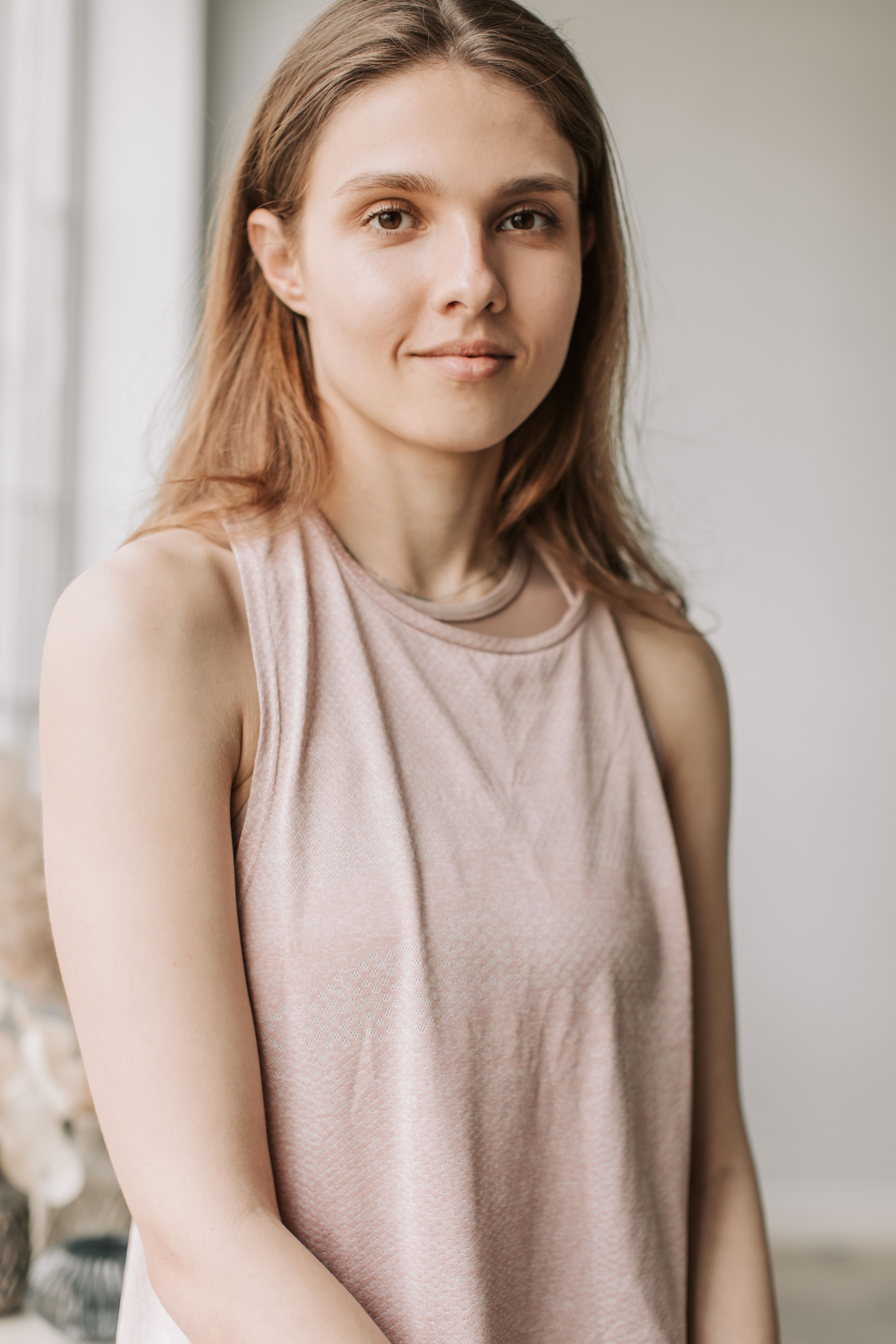 Elegant portrait of a young woman smiling in a well-lit indoor setting, wearing a beige tank top.