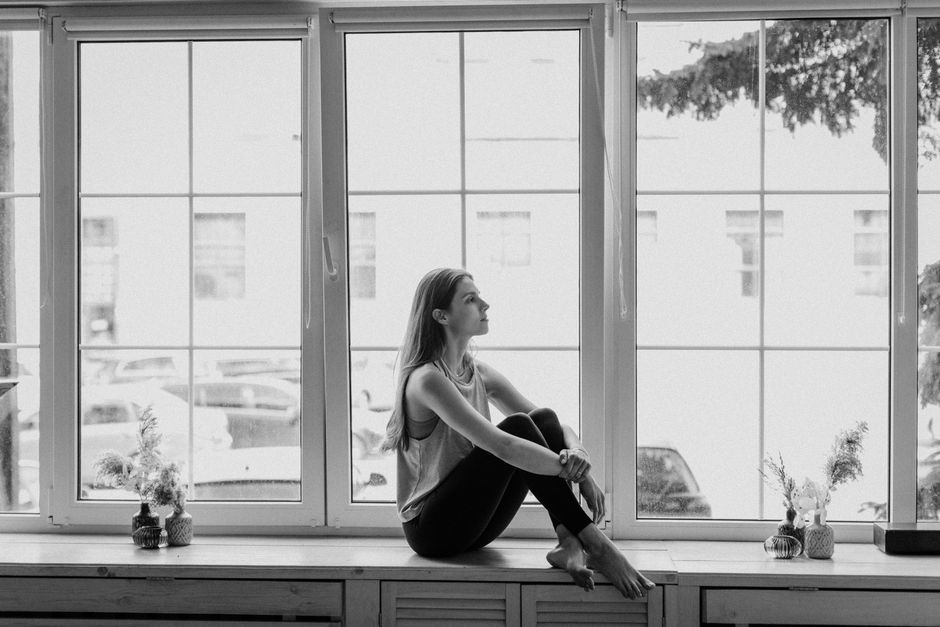 Black and white photo of a young woman sitting on a windowsill and deep in thought.