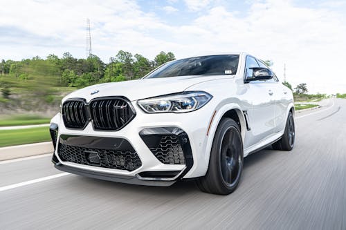 Long exposure of big luxury white contemporary automobile riding through paved road next to woodland