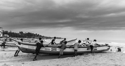 Grayscale Photo of People Pushing a Boat