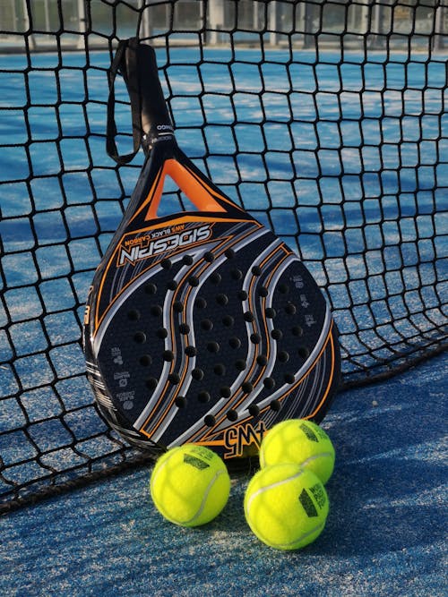 From above of padel racket and small colorful balls near fence on sports ground