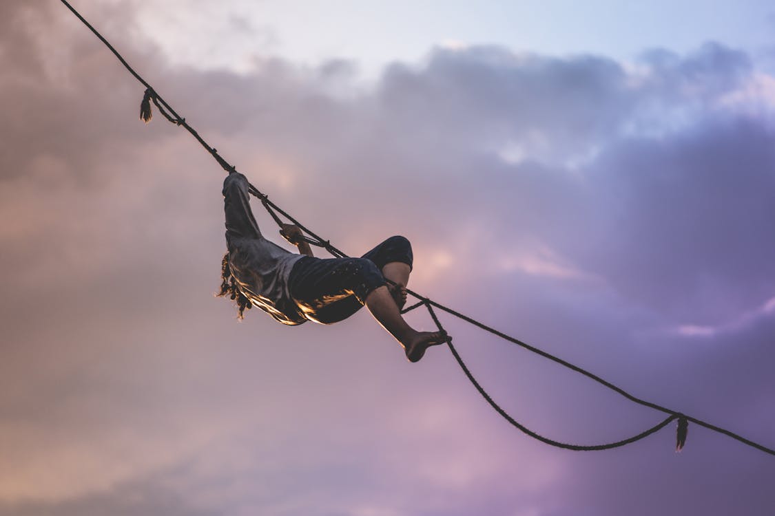 Free Unrecognizable male athlete climbing tightrope under cloudy sky Stock Photo