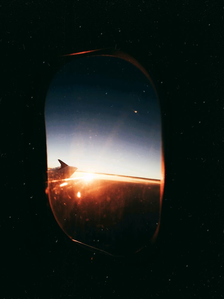 View From Inside Airplane Window At Shiny Sky At Sunset