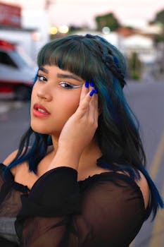 Portrait of a fashionable young woman with blue hair posing on a street in vibrant makeup.