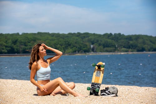 Free Sensual dreamy model resting on beach near sea and skateboard Stock Photo
