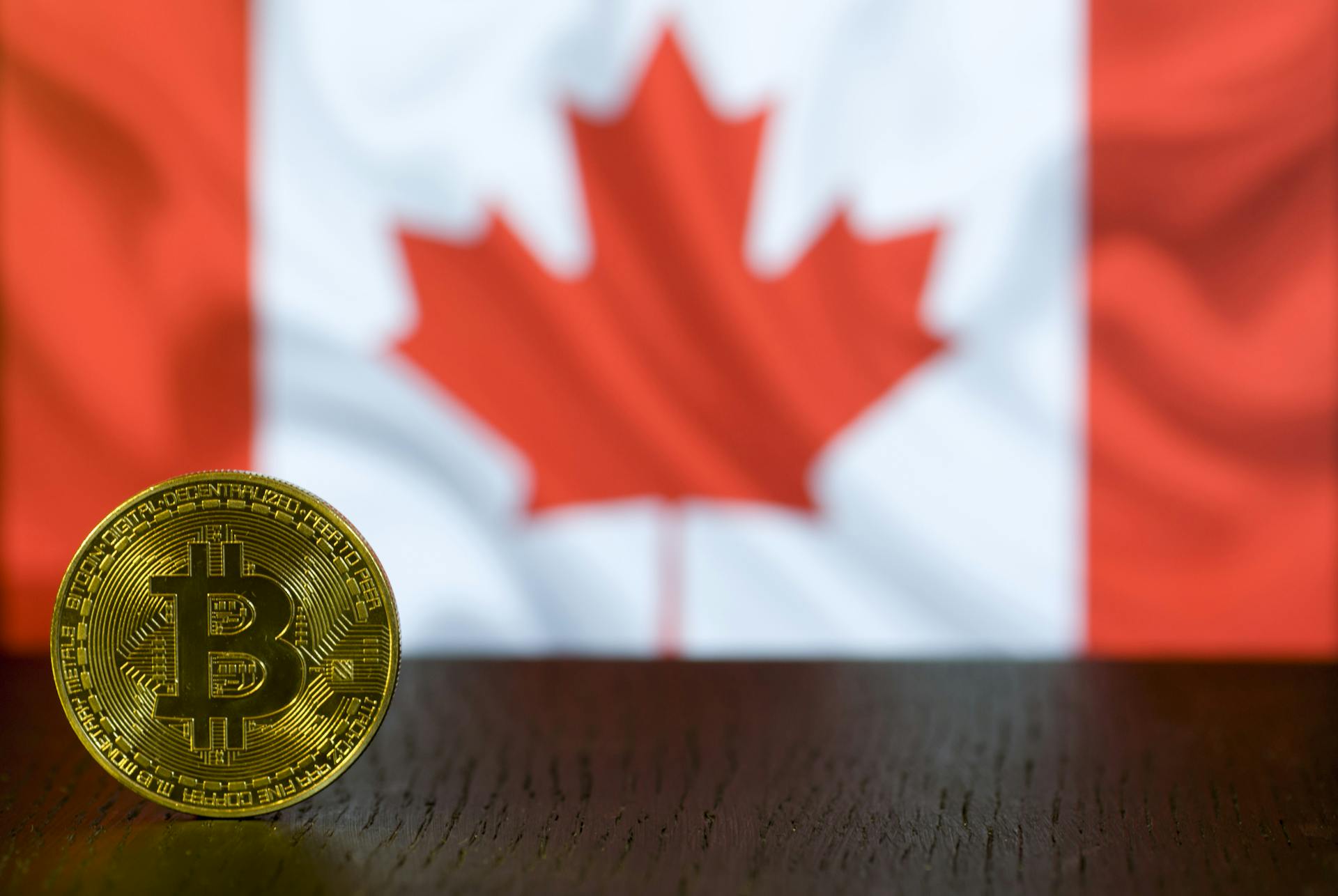 Golden Bitcoin coin displayed in front of a blurred Canadian flag symbolizing cryptocurrency in Canada.