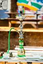 Colorful hookah with green hose on table near cup and transparent jars with dry herbs on table in cafeteria