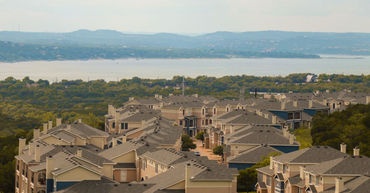 From above of aged housing complex near trees and river with mounts behind under cloudy sky