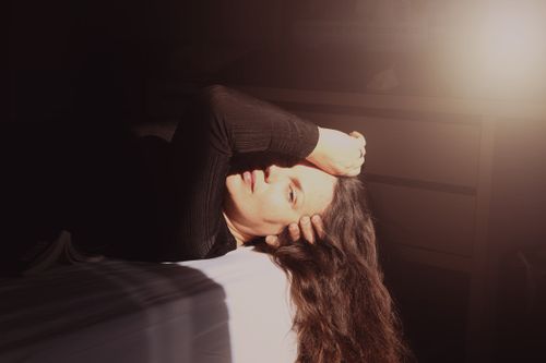 Free Side view of female covering half face with arm while lying in bed at home and looking at camera Stock Photo