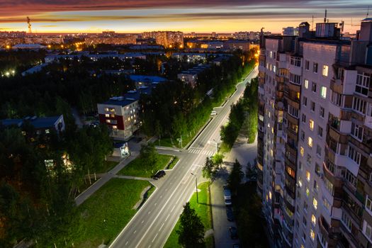 From above of asphalt roadway between multistage dwelling building exteriors under bright sky at sunset