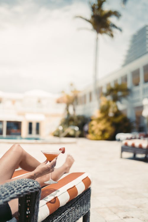 Free Woman Holding Martini Glass While Lying on Orange Beach Lounge Chair Stock Photo