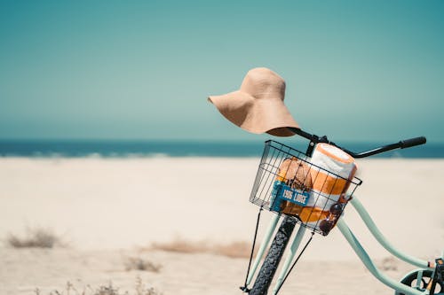 Person in Brown Sun Hat and Black Backpack Holding Blue and White Basket on Beach during