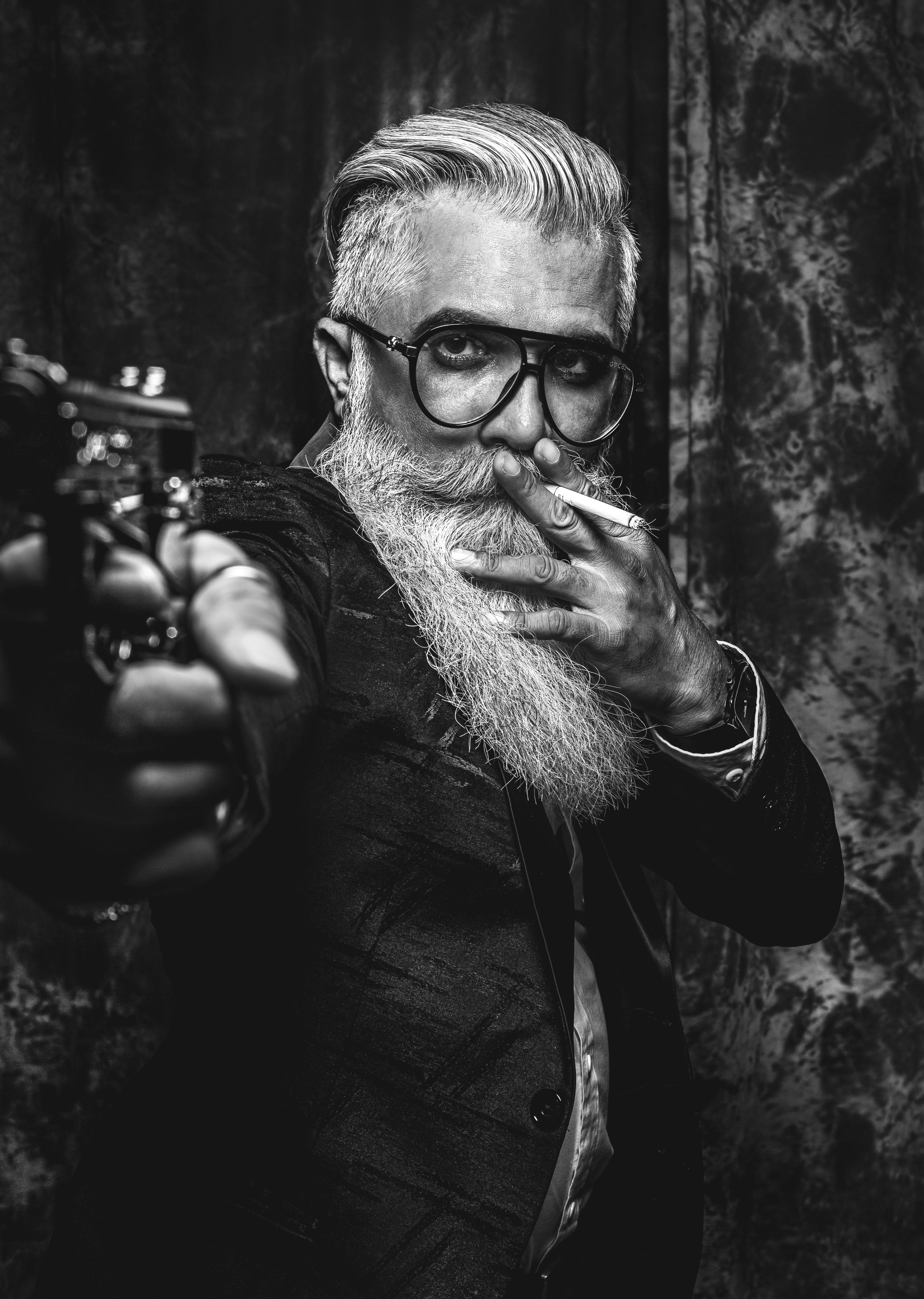 grayscale photo of man wearing eyeglasses holding a gun