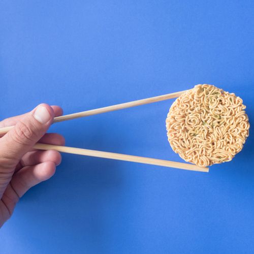 Free From above of faceless person holding delicious raw noodles with chopsticks placed on blue surface Stock Photo