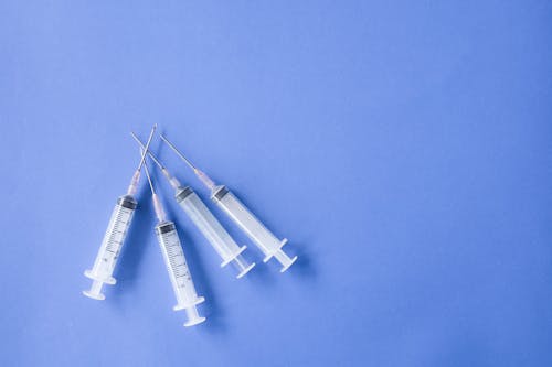 Top view flat lay composition of heap of medical syringes arranged on blue surface