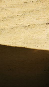 Yellow brick wall with dramatic shadow casting across the surface on a sunny day.