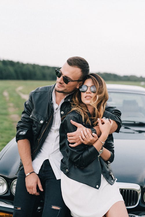 Stylish couple in sunglasses embracing near luxury car in countryside