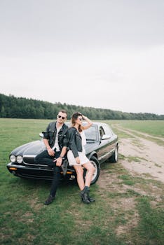一对穿着皮夹克的时尚情侣，在一望无际的田野上与一辆老式黑色汽车合影