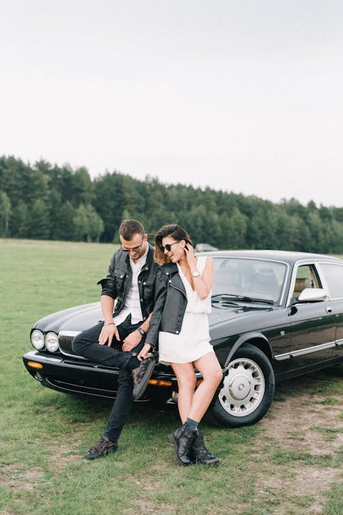 A Couple Sitting on Black Car on the Grass Field