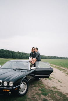 Fashionable couple in black leather jackets sitting on a vintage car outdoors, enjoying a moment together.