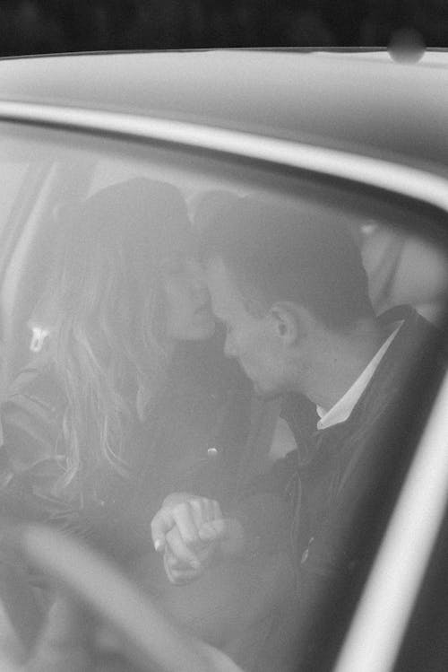 Grayscale Photo of Man and Woman Kissing Inside the Car