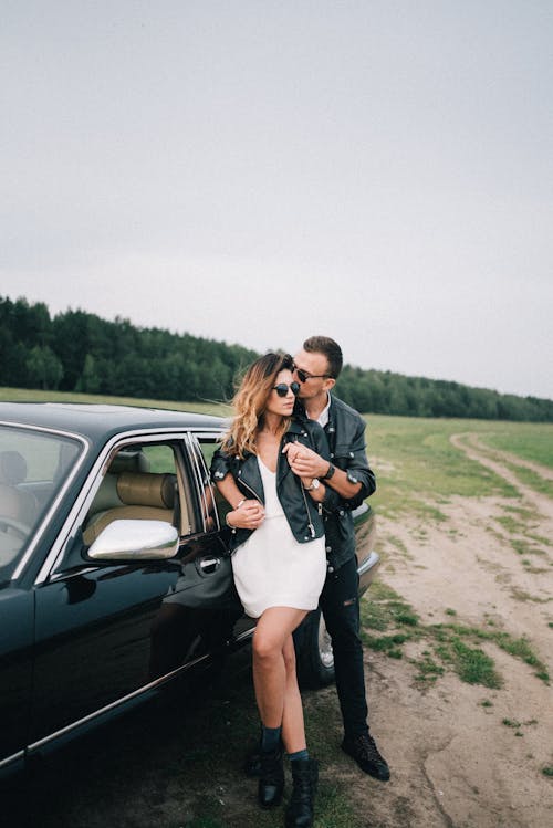 An Affectionate Couple Standing by a Black Car in the Countryside 