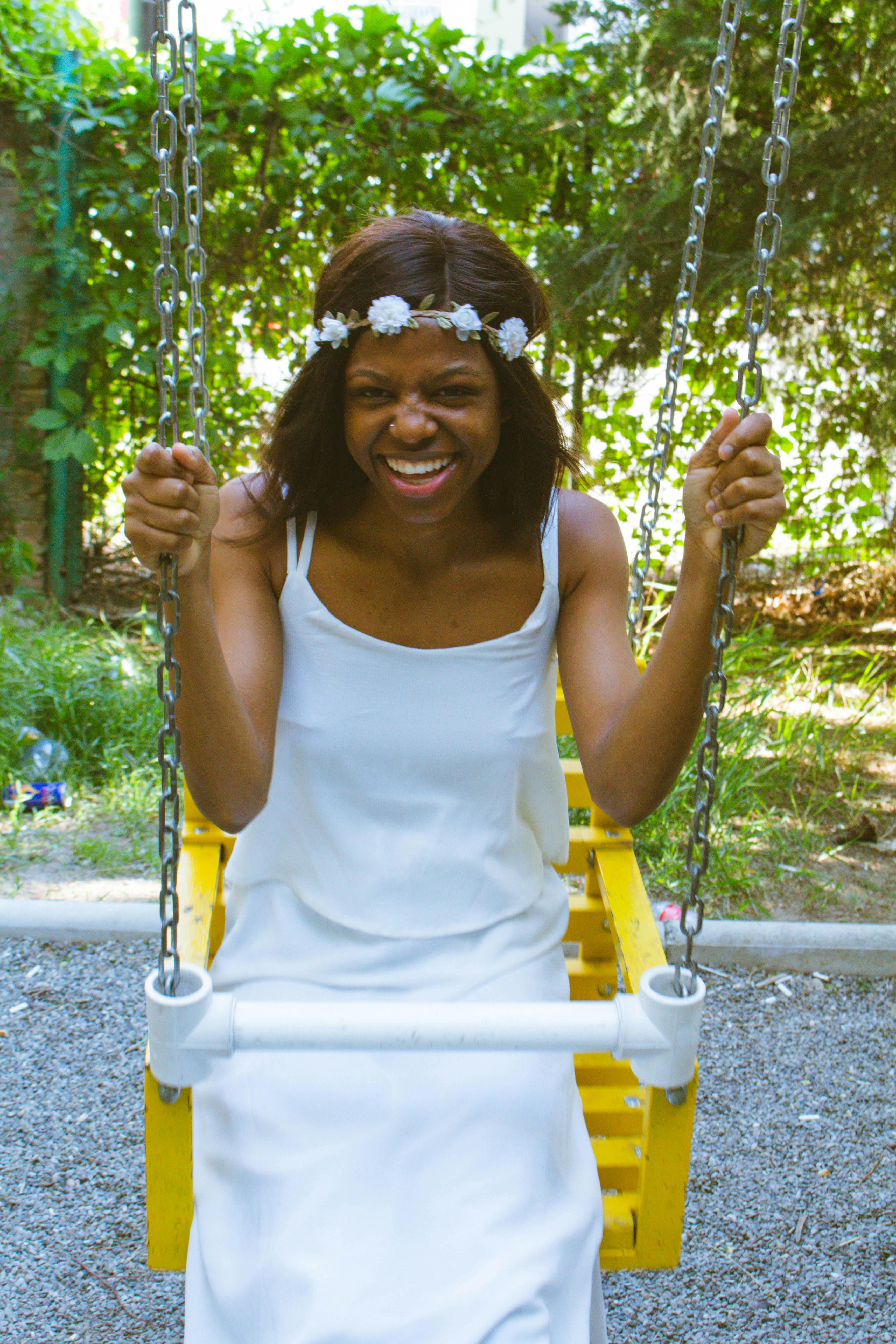 cheerful young black female sitting on swing and laughing in park