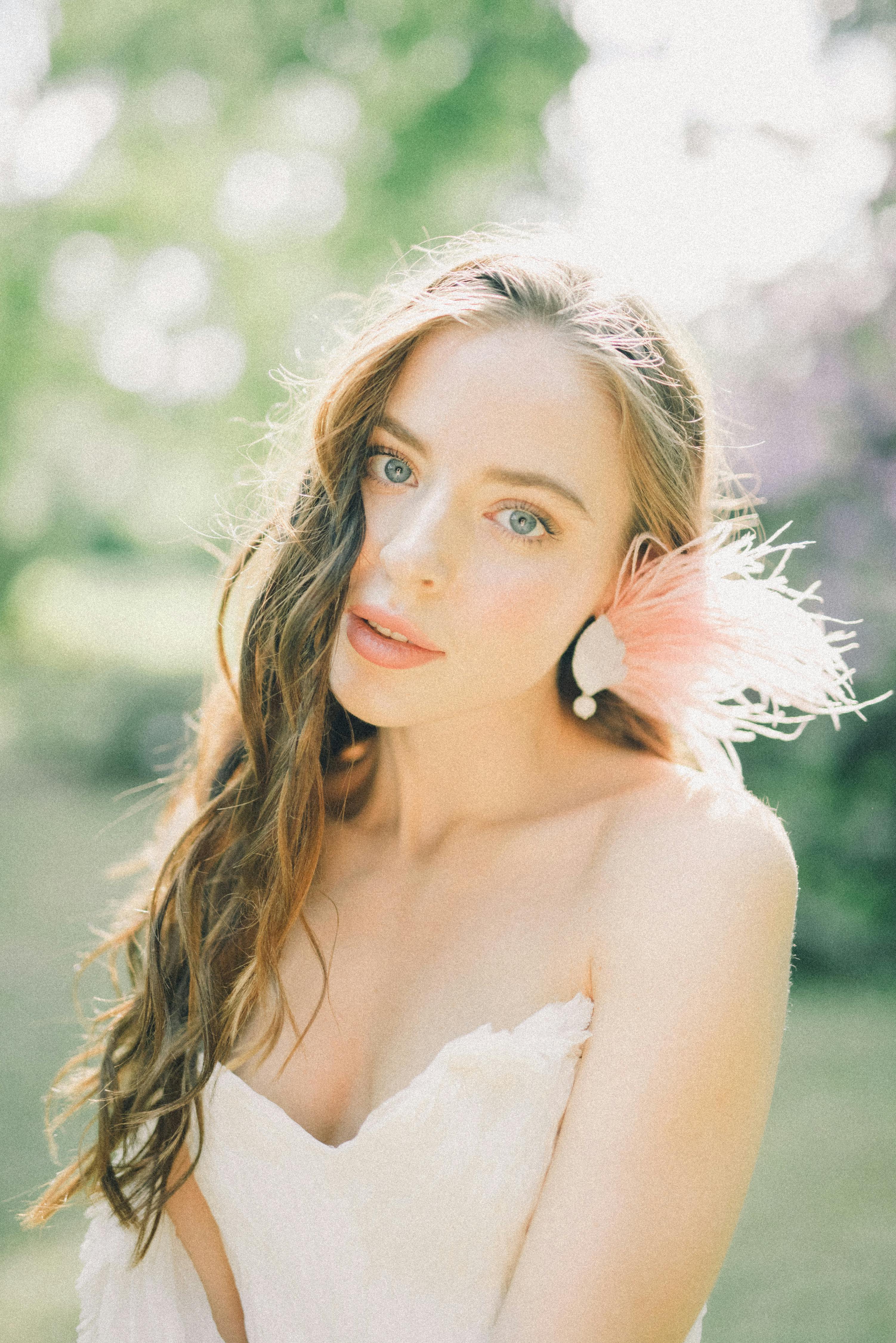 一位美丽的女人身着白色连衣裙，头戴羽毛配饰，在户外柔和的阳光下摆着姿势