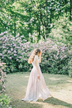 An elegant woman in a pink dress walking through a vibrant, flower-filled garden in spring.